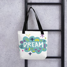 Load image into Gallery viewer, A white tote bag with black handles handing on a black ladder. The bag features a design with the word &#39;dream&#39; with an illustrated cloud around the word with colorful sketchy around. 