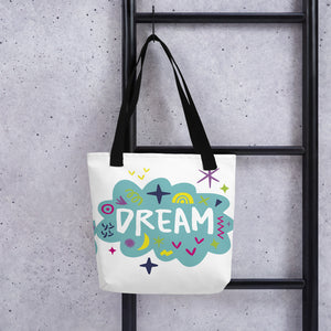 A white tote bag with black handles handing on a black ladder. The bag features a design with the word 'dream' with an illustrated cloud around the word with colorful sketchy around. 