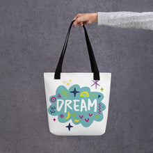 Load image into Gallery viewer, A person holding a white tote bag with black handles. The bag features a design with the word &#39;dream&#39; with an illustrated cloud around the word with colorful sketchy around. 