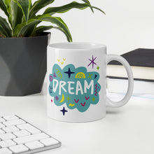 Load image into Gallery viewer, A white mug on a desktop. The mug features a design with the word &#39;dream&#39; in an illustrated cloud with sketchy elements around it. 