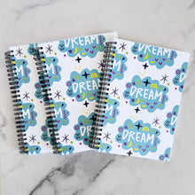 Load image into Gallery viewer, Three spiral notebooks are on a tabletop. The white spiral notebooks have black spiral binding. The pattern design features the word &quot;dream&quot; inside a cloud shape with sketchy elements around. 