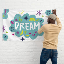 Load image into Gallery viewer, A man hanging a large flag on a white brick wall. The white flag features a pattern with the word &quot;dream&quot; featured inside a cloud with sketchy illustrations around the word. 