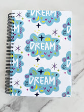 Load image into Gallery viewer, A spiral notebook is on a tabletop. The white spiral notebook has black spiral binding. The pattern design features the word &quot;dream&quot; inside a cloud shape with sketchy elements around. 