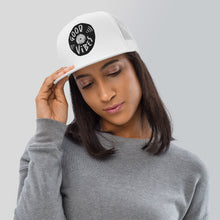 Load image into Gallery viewer, A woman in a gray shirt wearing a white trucker hat. The hat features an black embroidered design with an illustrated vinyl record and the words &#39;good vibes&#39; inside.  