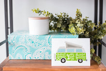 Load image into Gallery viewer, A greeting card is on a table top with a present in blue wrapping paper in the background. On top of the present is a candle and some greenery from a plant too. The card features the words “Difficult roads often lead to beautiful destinations” with an illustrated campervan.