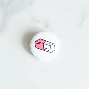 A button pin on a white tabletop. The button features an illustration of an eraser. 