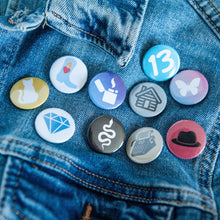 Load image into Gallery viewer, A photo of 10 pin badges on a jean jacket. The badges feature illustrations of a snake, a lighter, a cowboy boot,  cat, a butterfly, a house, a typewriter, a diamond, the number 13, and a black hat. 