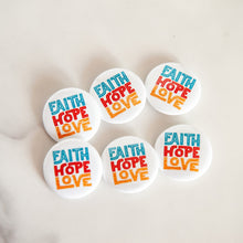 Load image into Gallery viewer, Buttons on a white tabletop. The buttons feature word art illustrations with the words &quot;Faith Hope Love.&quot; 