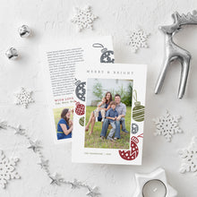 Load image into Gallery viewer, A photo of a double-sided Christmas card showing the front and back of the card laying on a white surface. Around the two sides of the card are surrounded with white snowflake ornaments, silver bells, a silver reindeer, white tea light snowflake candle and silver star garland. The front of the card features a photo with the words Merry &amp; Bright at the top and illustrated ornaments around the photo. The back of the card features two photos, illustrated ornaments and space to write a family update.
