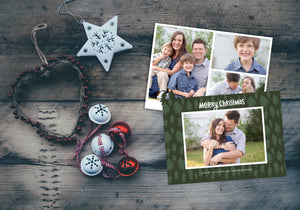 A photo of a Christmas card showing the front and back of the card laying on a wood surface. To the left of the cards are some ornaments. The front of the card features a photo with a frame around it with illustrated pine trees. Above the photo reads “Merry Christmas” and below the photo you can add your family name. The back of the card features three photos with illustrated pine trees. 