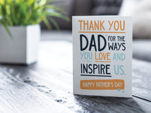 Load image into Gallery viewer, A greeting card is featured on a desktop with a green plant to the side. The card features the words  &quot;Thank You Dad for the ways you love and inspire us. Happy Father&#39;s Day.” 