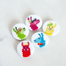 Load image into Gallery viewer, A set of five buttons on a white tabletop. The buttons feature five different colorful, illustrated llamas. 