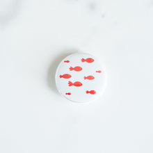 Load image into Gallery viewer, A button on a white tabletop. The button features an illustration of a school of fish. 