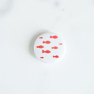 A button on a white tabletop. The button features an illustration of a school of fish. 