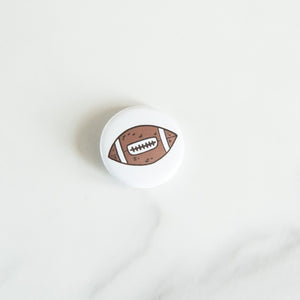 A buttons on a white tabletop. The button features an illustrations of an American football. 