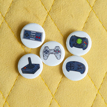 Load image into Gallery viewer, A set of five button pins on a yellow background. The buttons feature five different illustrations of game controllers. 