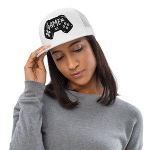 A woman in a gray shirt wearing a white trucker hat. The hat features an embroidered design with an illustrated game controller with the word 'gamer' inside the illustration.  