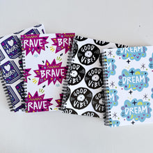 Load image into Gallery viewer, A set of four spiral bound notebooks. The notebooks feature a pattern design  with the words brave, dream, good vibes and I love books. 