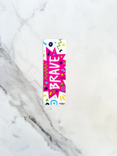 Load image into Gallery viewer, A bookmark with the word &quot;brave&quot; in white within a star-like pink shape with fun, sketchy elemts around. The bookmark is on a tabletop.