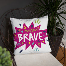 Load image into Gallery viewer, A white pillow on a chair with plants around. The white pillow features the artwork on a white background with a hot pink star with the word &#39;brave&#39; inside and sketchy, fun elements around the word. 