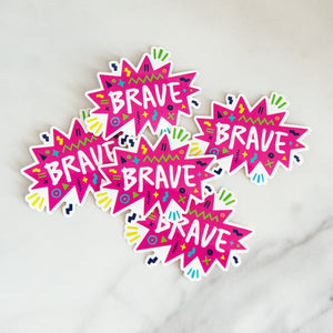 Vinyl die cut stickers with the word "brave" featured inside a pink star-like shape with fun sketchy elements around it. 