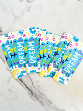 Load image into Gallery viewer, A group of bookmarks on a tabletop. The bookmark design has the word &quot;dream&quot; inside a teal cloud-like shape with sketchy, whimsical items around. 