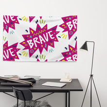 Load image into Gallery viewer, A large flag is featured hanging on the wall of an office placed above a desk. The white flag features a pattern with the word &quot;brave&quot; featured inside a pink star-like shape with sketchy illustrations around the word. 