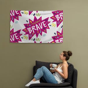 A large flag is featured hanging on the wall with a woman sitting on a sofa below it. The white flag features a pattern with the word "brave" featured inside a pink star-like shape with sketchy illustrations around the word. 