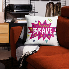 Load image into Gallery viewer, A white pillow on a red sofa. The white pillow features the artwork on a white background with a hot pink star with the word &#39;brave&#39; inside and sketchy, fun elements around the word. 