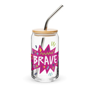 A photo of a glass can tumbler on a white background with a bamboo lid and silver metal straw. The design on the glass tumbler says the word "brave" inside a hot pink star with illustrated sketchy elements around the word. 