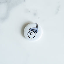 Load image into Gallery viewer, A buttons on a white tabletop. The button features an illustrations of a golf club with ball. 