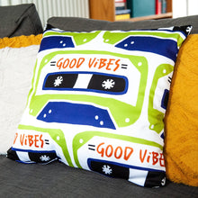 Load image into Gallery viewer, A white pillow on a grey sofa with other pillows. The white pillow features the artwork on a white background with an illustrated cassette tape pattern with the words &#39;good vibes.&#39;