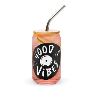 A photo of a glass can tumbler on a white background with a bamboo lid and silver metal straw. The design on the glass tumbler says the words "good vibes" inside an illustrated vinyl record.