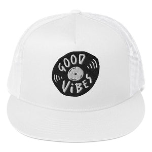 A white trucker hat on a white background showing a close up of the hat. The hat features an black embroidered design with an illustrated vinyl record and the words 'good vibes' inside.  