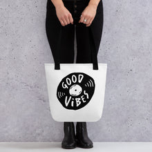 Load image into Gallery viewer, A person holding a white tote bag with black handles. The bag features a design with the words &#39;good vibes&#39; inside an illustrated vinyl record. 