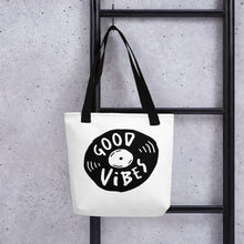 Load image into Gallery viewer, A white tote bag with black handles handing on a black ladder. The bag features a design with the words &#39;good vibes&#39; inside an illustrated vinyl record. 