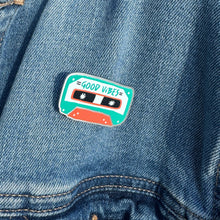 Load image into Gallery viewer, An enamel pin featuring the words &quot;good vibes&quot; inside an illustrated cassette tape. The pin is on a jean jacket.