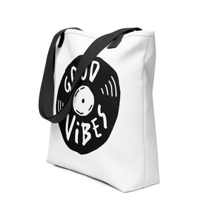 A side view of a white tote bag with black handles on a white background. The bag features a design with the words 'good vibes' inside an illustrated vinyl record. 