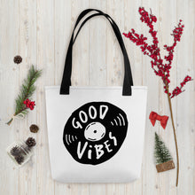 Load image into Gallery viewer, A white tote bag with black handles on a wood tabletop with Christmas items around it. The bag features a design with the words &#39;good vibes&#39; inside an illustrated vinyl record. 