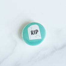 Load image into Gallery viewer, A button on a white tabletop. The button features an illustration of a grave with RIP on it.