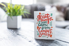 Load image into Gallery viewer, A greeting card featured on a black, wood coffee table. There’s a white planter in the background with a green plant. There’s also a gray sofa in the background with a white pillow. The card features the words “Great things never came from comfort zones.”