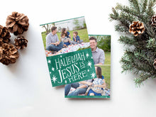 Load image into Gallery viewer, A photo of a double-sided Christmas card showing the front and back of the card laying on a white surface. Around the two sides of the card are pine cones and pine needles. The front of the card features a photo on the top and on the bottom is in green with words in white “Hallelujah Jesus is Here” with white stars around it. The back of the card features two photos.
