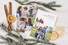 Load image into Gallery viewer, A photo of a double-sided Christmas card showing the front and back of the card laying on a white surface. Around the two sides of the card are pine needles, cinnamon sticks and dried oranges. The front of the card features a photo on the bottom and on the top it reads “Happy Holidays, The Franklins” with illustrated modern pine trees. The back of the card features three photos.