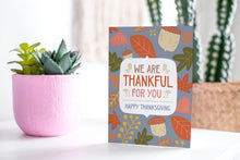 Load image into Gallery viewer, A greeting card featured standing up on a white tabletop with a pink plant pot with succulents. The card features the words &quot;We are Thankful for You, Happy Thanksgiving&quot; with illustrated leaves and acorns around the words. 