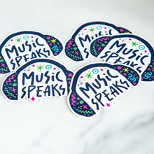 Load image into Gallery viewer, Vinyl die cut stickers with the words &quot;music speaks&quot; with illustrated headphones around the words. 