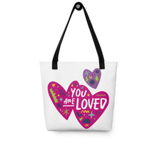 Load image into Gallery viewer, A white tote bag with black handles on a white background. The bag features a design with the words &#39;you are loved&#39; inside two illustrated pink hearts with a smaller, purple heart above. 