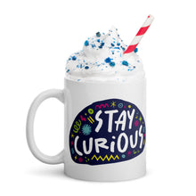 Load image into Gallery viewer, A white mug on a white background with whipped cream and a straw. The mug features a design with the words &#39;stay curious&#39; in an illustrated oval shape with sketchy elements around it. 