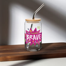 Load image into Gallery viewer, A photo of a glass can tumbler on a dark wood tabletop. The glass tumbler has a bamboo lid and silver metal straw. The design on the glass tumbler says the word &quot;brave&quot; inside a hot pink star with illustrated sketchy elements around the word. 