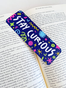 A bookmark placed inside a book. The bookmark has the words "stay curious" with fun, sketchy illustrations. 