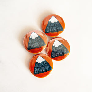 Buttons on a white tabletop. The buttons feature word art illustration with the words "Don't Give Up" with a mountain illustration.